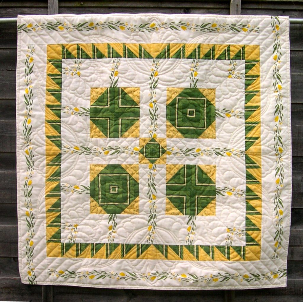 White quilt with green and yellow patchwork and hand quilting