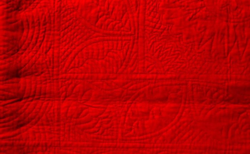 Red woolen quilt with hand-stitched quilting designs.