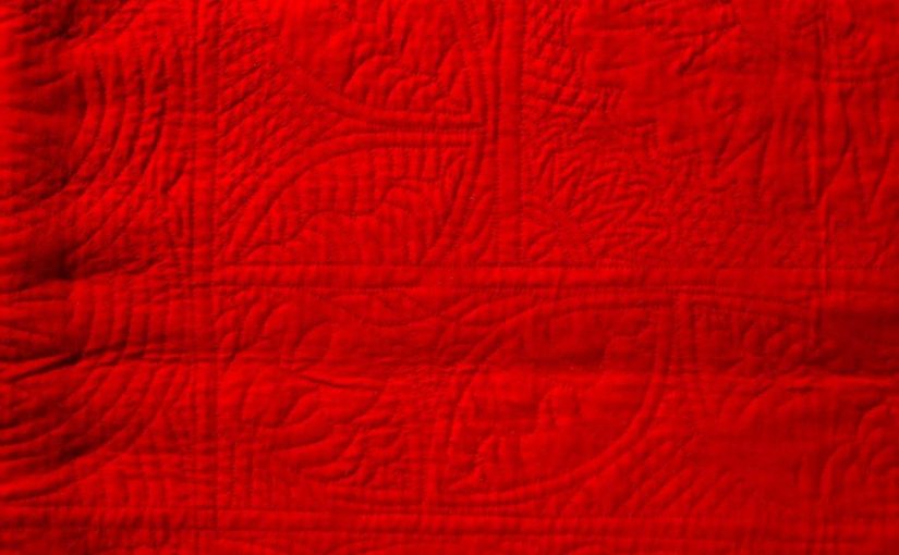 Red woolen quilt with hand-stitched quilting designs.