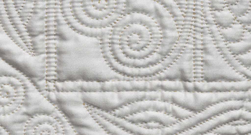 Yellow quilting on white sateen fabric. The stitching sinks into the satin weave only in the horizontal direction.