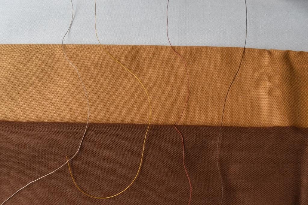 Four threads (grey, yellow, rust and dark brown) spread across three fabrics (white, sand, brown)