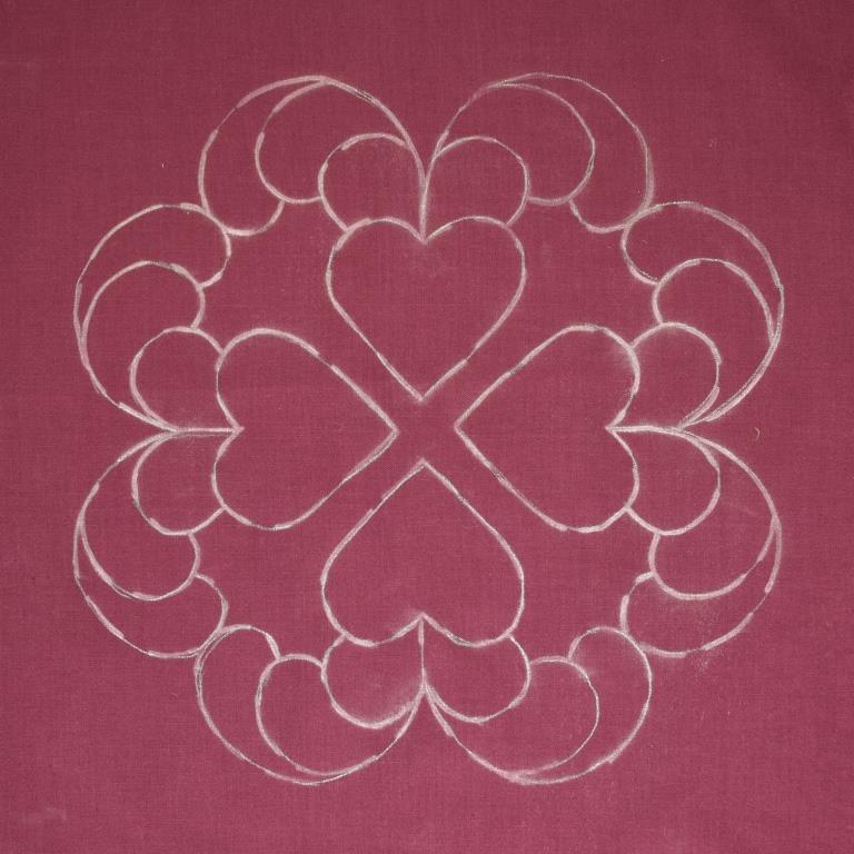 White chalky lines show the design of hearts and feathers on purple fabric.