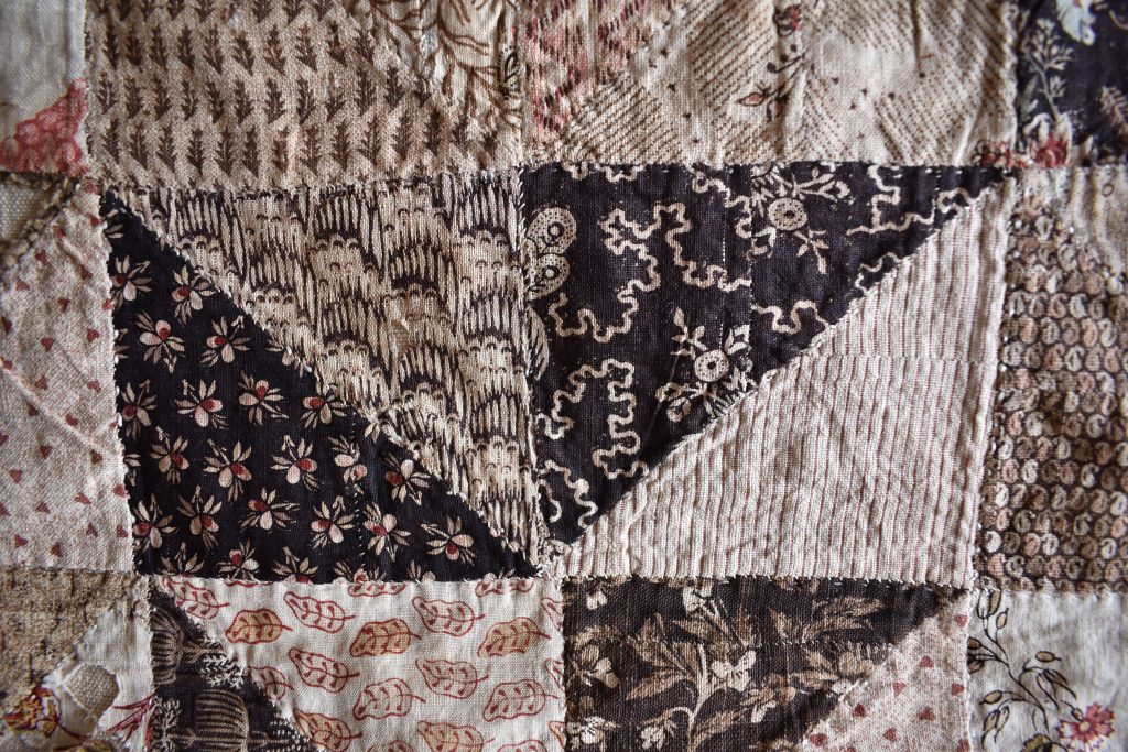 Small pieces of dark printed fabrics have been stitched together to make some of the triangles in this patchwork.