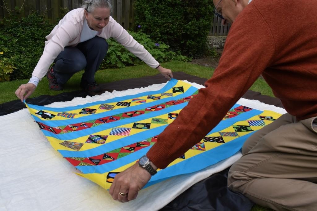 Two people laying quilt top down onto wadding