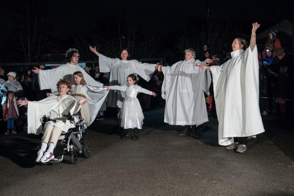 Five women and two children dressed as angels, with arms raised