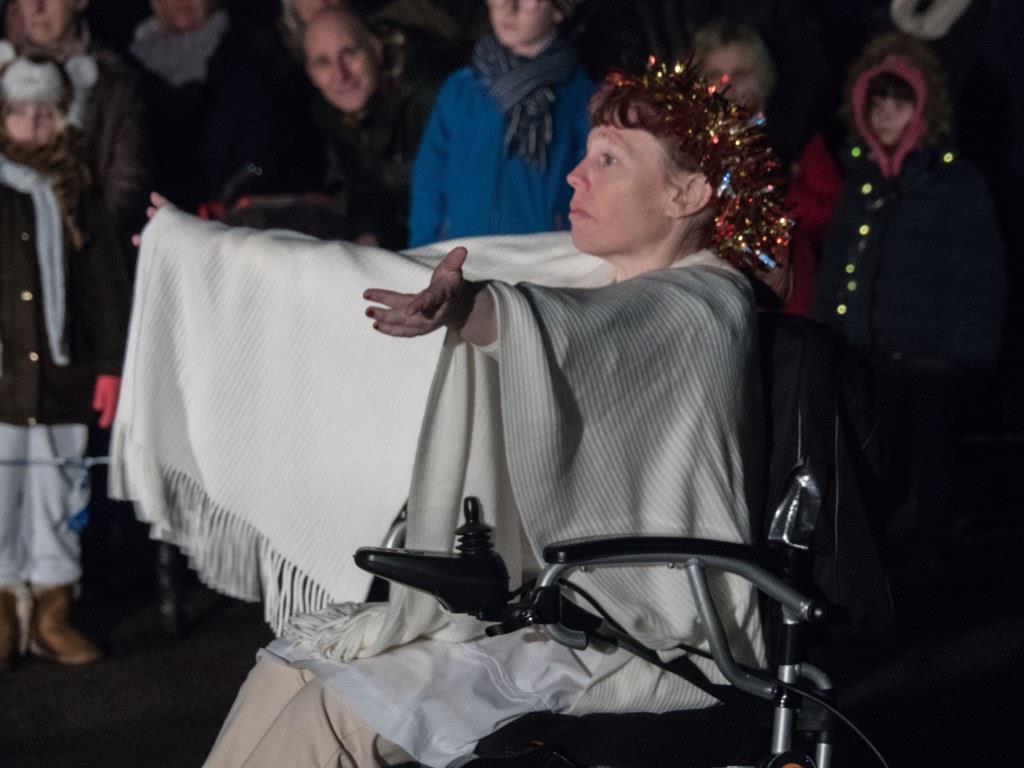 Woman dressed as angel, in wheelchair with outstretched arms.